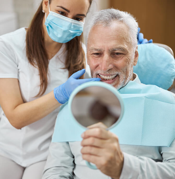 man looking at smile in the mirror at the dentist